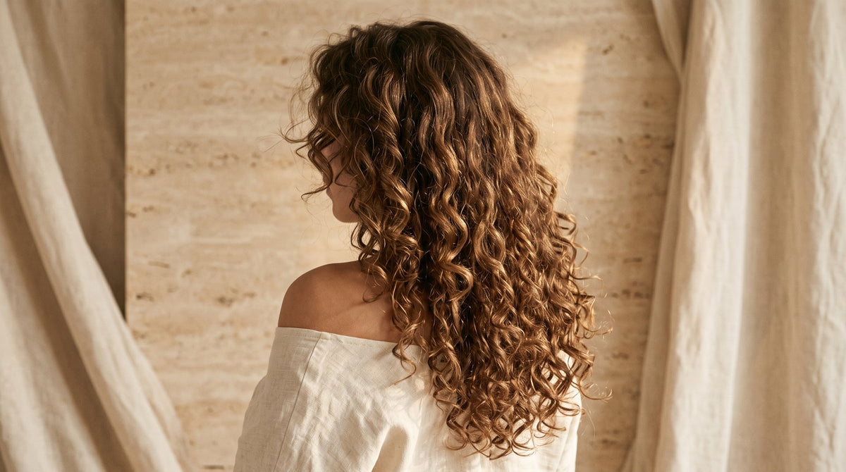 Long glossy brunette curly hair extensions with defined ringlets blended naturally, seen from behind