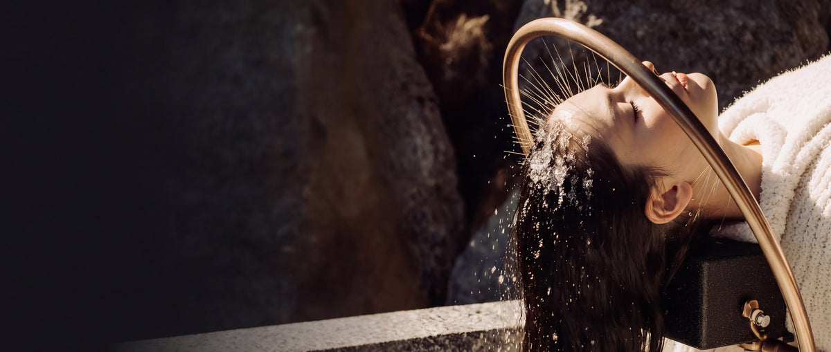 A woman relaxing at a Japanese head spa basin as a gold arched spray mists water over her scalp